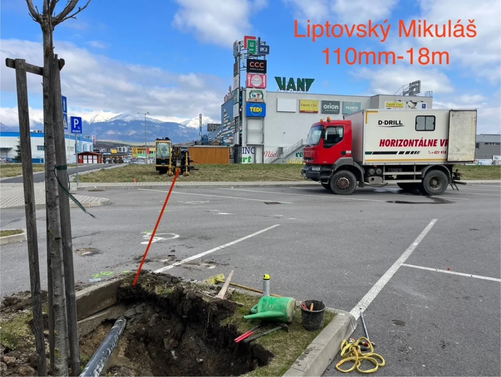 Jama v zelenom páse pri parkovisku obchodnej zóny v Liptovskom Mikuláši, v pozadí vozidlo D-Drill.
