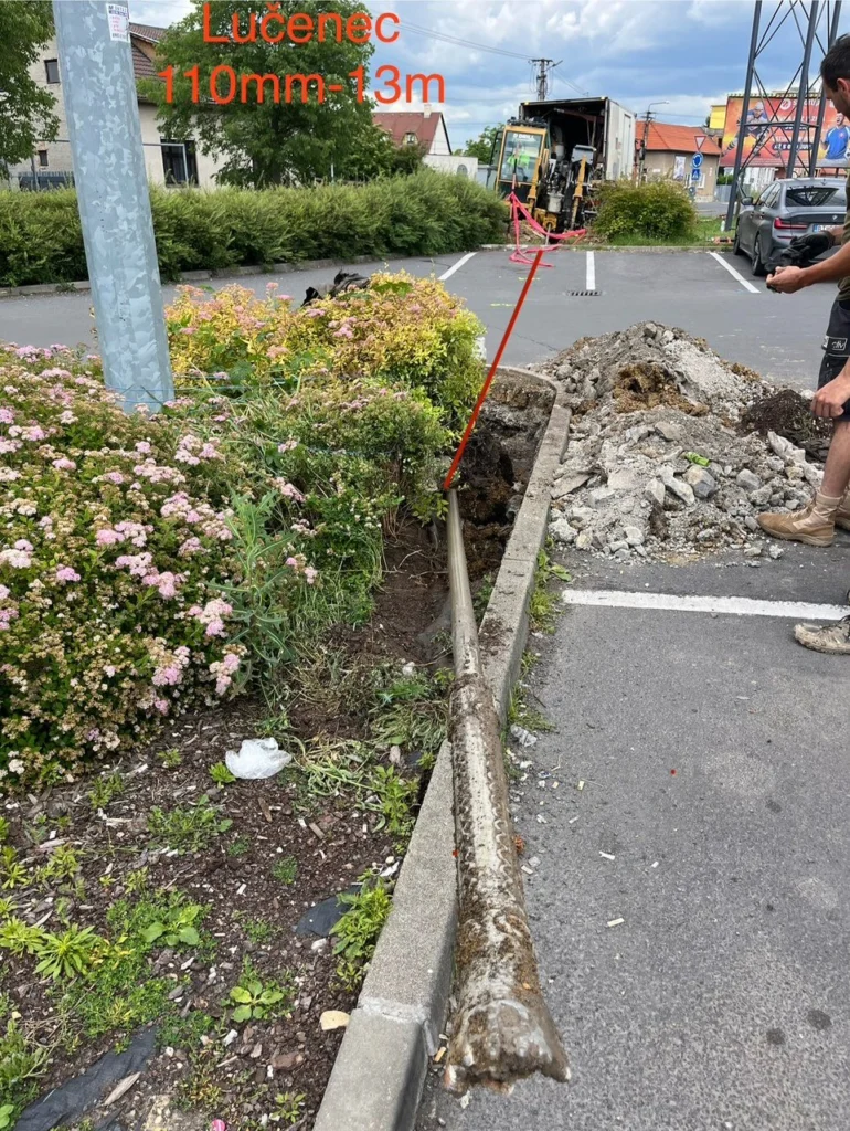 Potrubie zatiahnuté popod parkovisko v Lučenci, pri obrubníku a zelenom ostrovčeku.