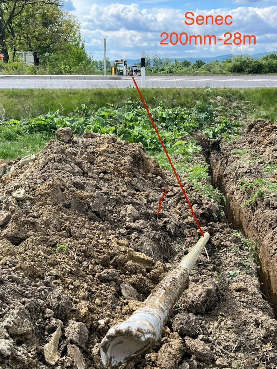 Potrubie Ø 200 mm zatiahnuté popod cestu v Senci, v pozadí cesta so zvodidlami a vrtná súprava.